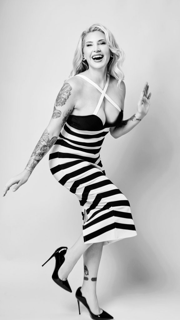 Black-and-white playful studio portrait of woman in striped dress and heels, mid-movement.