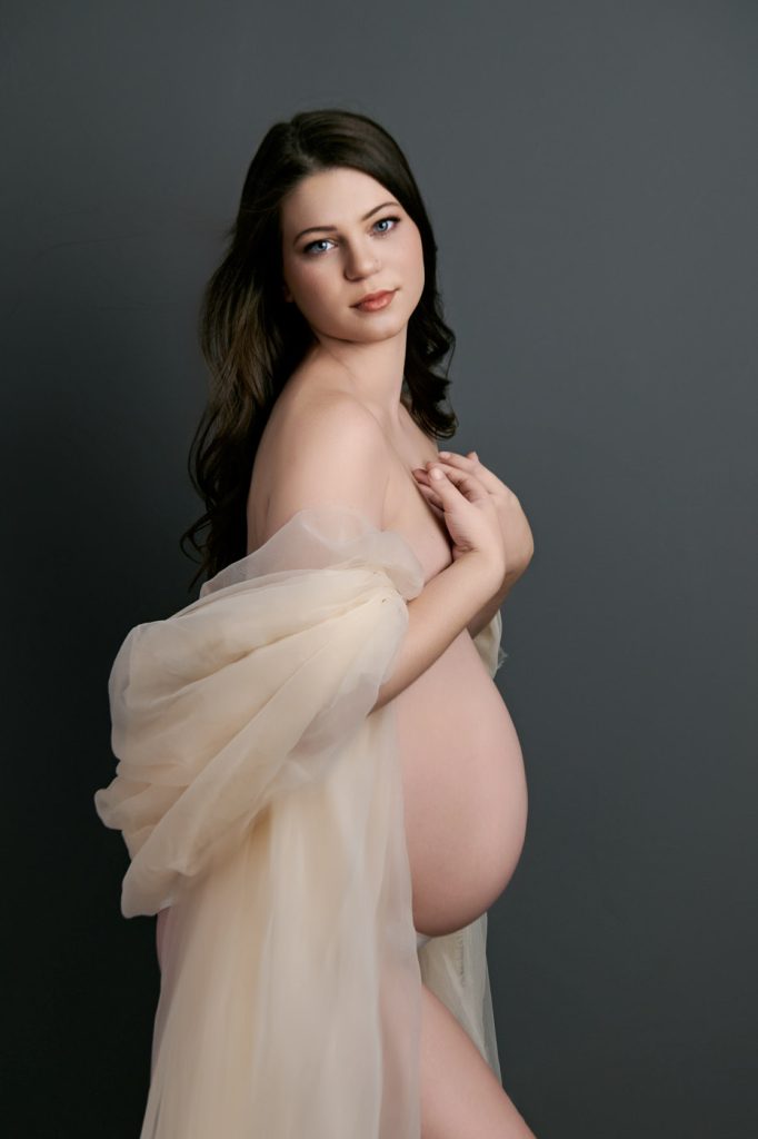 Maternity portrait of pregnant woman draped in soft fabric on a dark studio backdrop