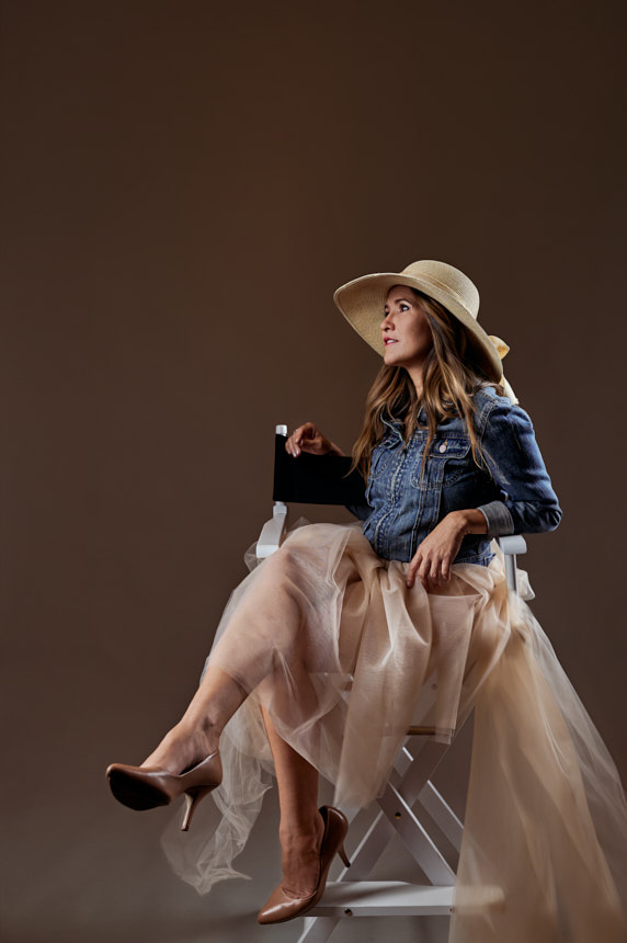 Editorial studio portrait of woman in wide-brim hat sitting in a director chair, Ocala Florida.